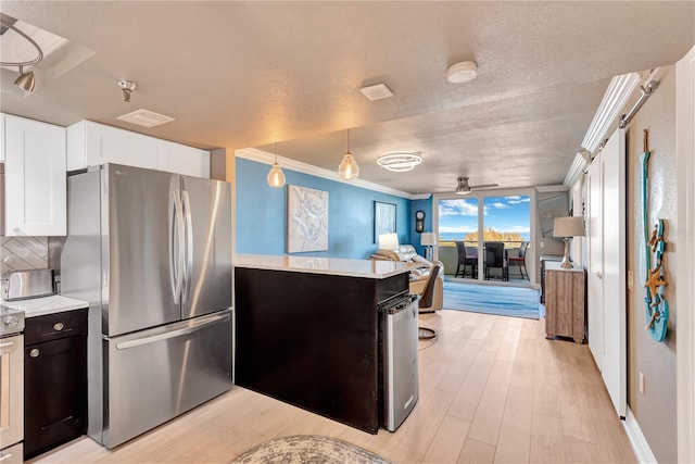 kitchen with pendant lighting, light countertops, ornamental molding, freestanding refrigerator, and white cabinets