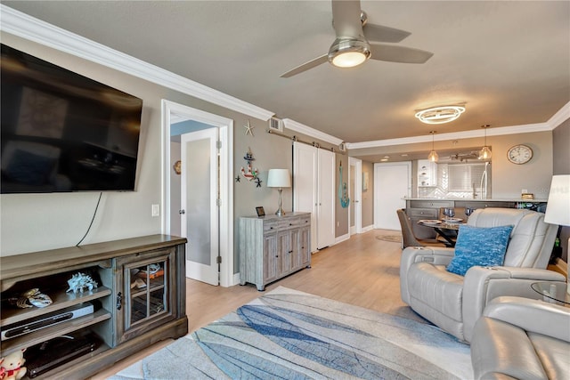 living room with light wood-style flooring, ceiling fan, crown molding, and a barn door