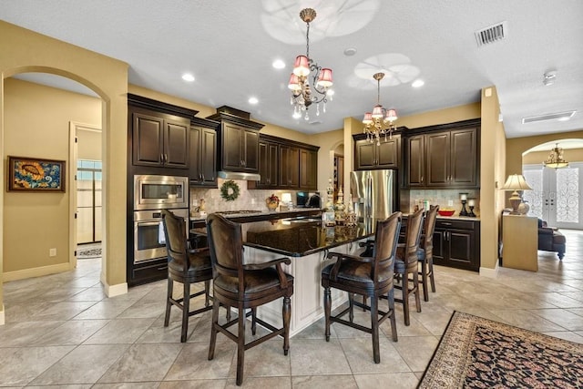 kitchen featuring dark brown cabinets, arched walkways, stainless steel appliances, and a breakfast bar area