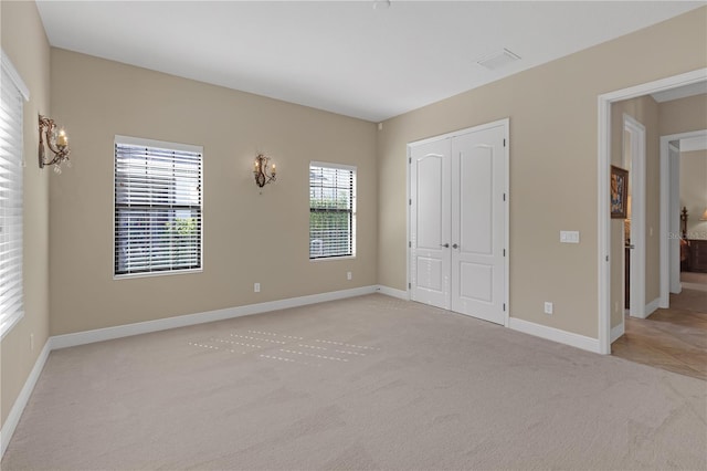 unfurnished bedroom featuring light carpet, a closet, visible vents, and baseboards