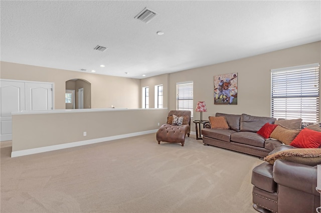 living area featuring arched walkways, visible vents, light carpet, and baseboards