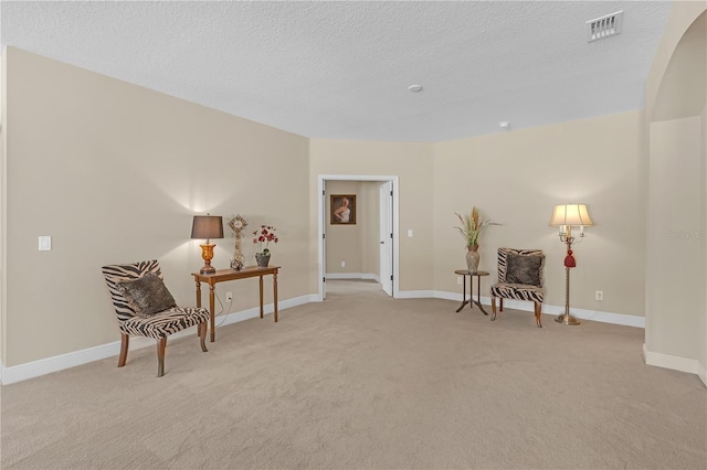 sitting room featuring a textured ceiling, light carpet, visible vents, and baseboards