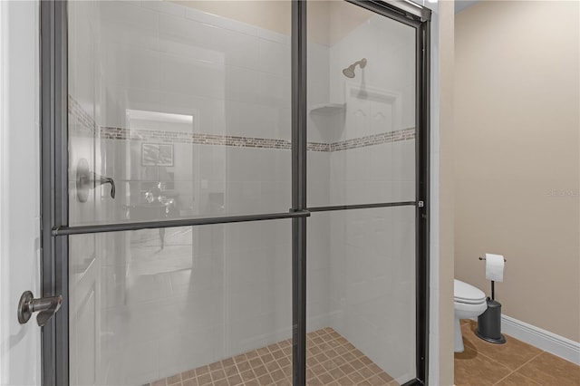 bathroom with toilet, a shower stall, baseboards, and tile patterned floors