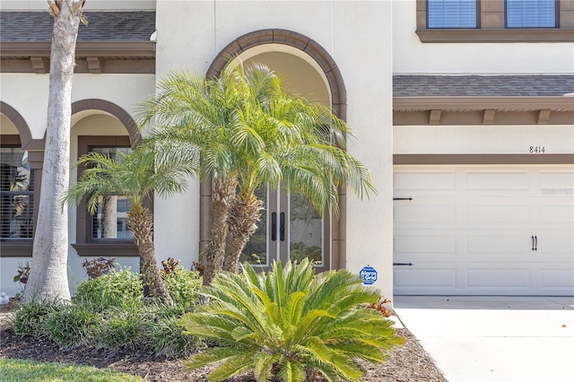 property entrance with a garage, stucco siding, and roof with shingles