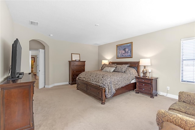 bedroom featuring arched walkways, light carpet, visible vents, and baseboards