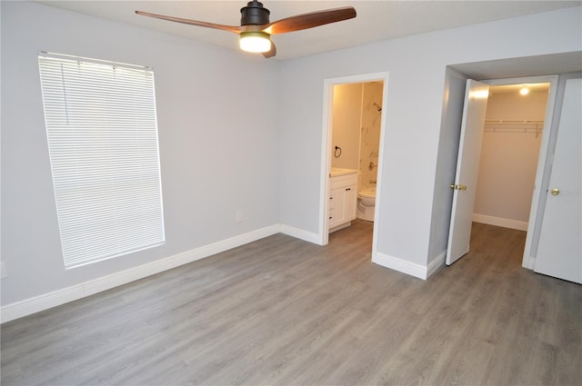 unfurnished bedroom featuring a closet, ensuite bath, ceiling fan, light hardwood / wood-style floors, and a walk in closet