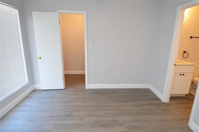 unfurnished bedroom with multiple windows, ensuite bathroom, and hardwood / wood-style floors