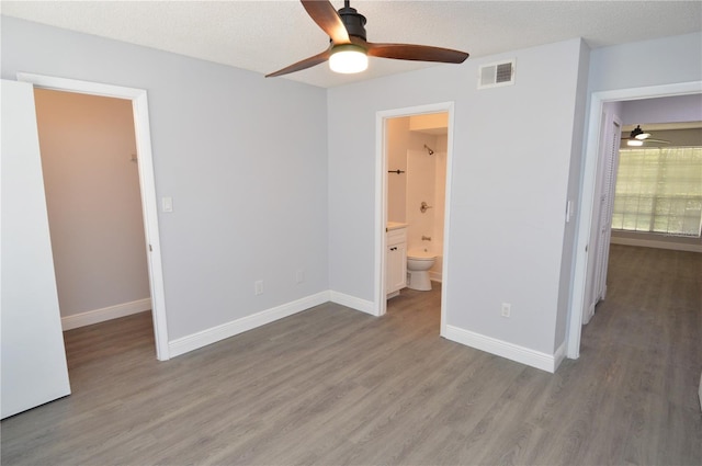 unfurnished bedroom with ensuite bath, wood-type flooring, a textured ceiling, and a walk in closet