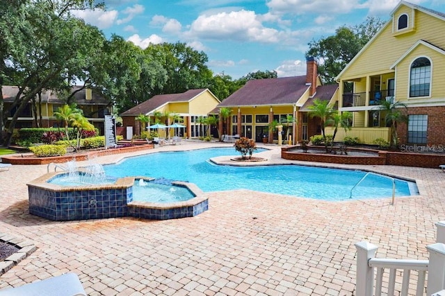 view of swimming pool with pool water feature and a hot tub