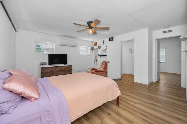 bedroom with hardwood / wood-style flooring, ceiling fan, and a wall mounted AC