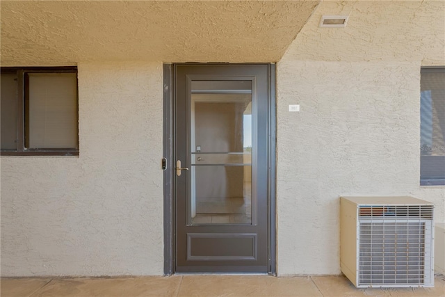 view of exterior entry featuring central air condition unit, stucco siding, and visible vents