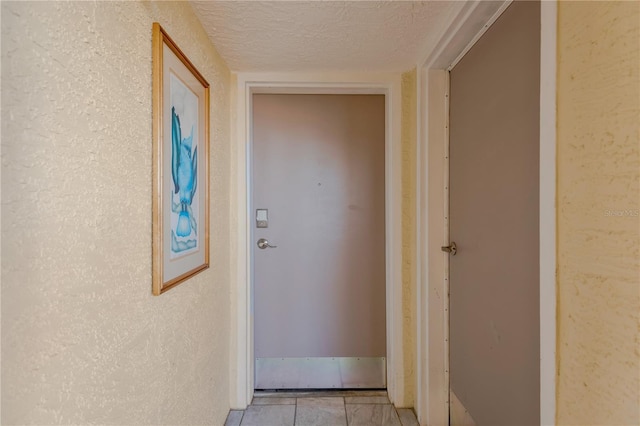 hall featuring light tile patterned floors, a textured ceiling, and a textured wall