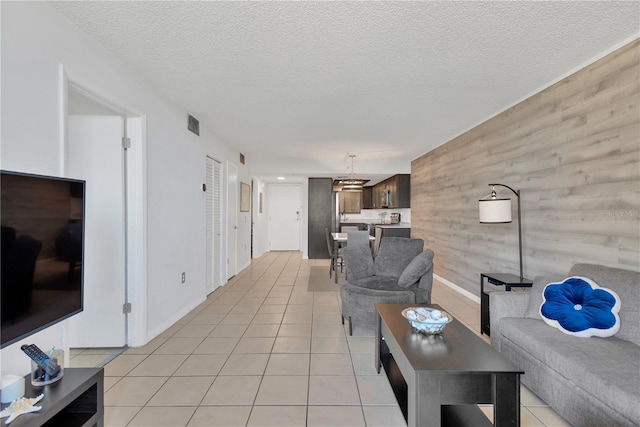 living room featuring light tile patterned flooring, visible vents, a textured ceiling, and wooden walls