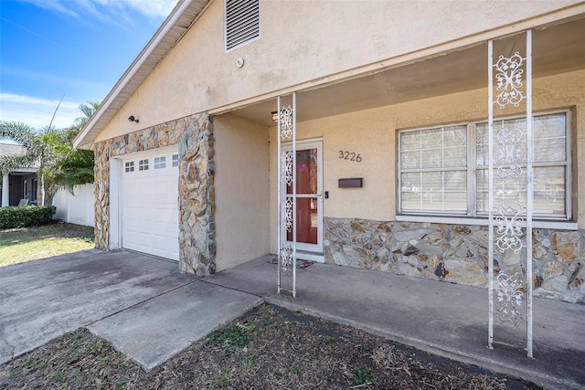 doorway to property featuring stone siding, an attached garage, and stucco siding