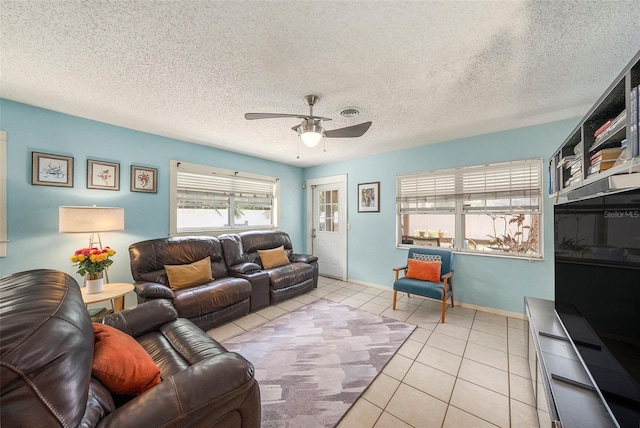 living area with light tile patterned floors, ceiling fan, baseboards, and a textured ceiling