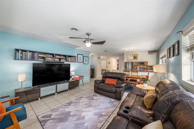 living area featuring light tile patterned floors, ceiling fan, visible vents, and a textured ceiling