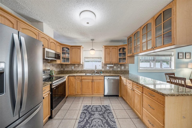 kitchen featuring appliances with stainless steel finishes, pendant lighting, glass insert cabinets, and a sink