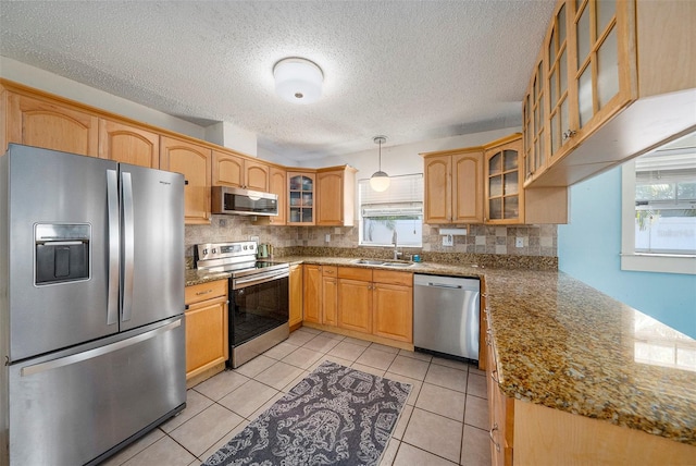 kitchen with decorative light fixtures, a sink, appliances with stainless steel finishes, light stone countertops, and glass insert cabinets