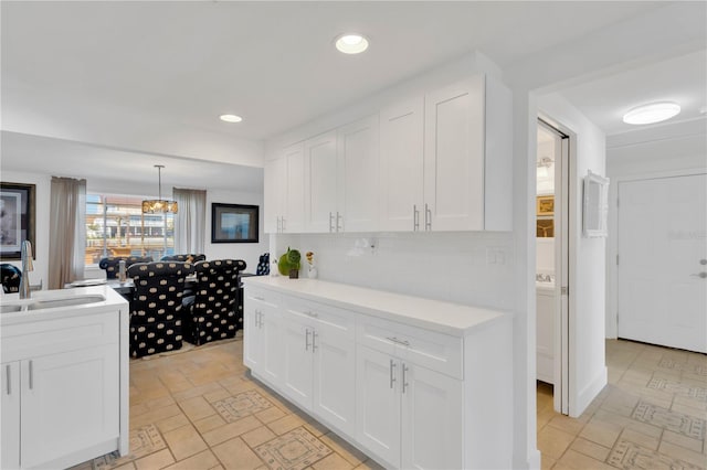 kitchen with white cabinetry, light countertops, backsplash, and a sink