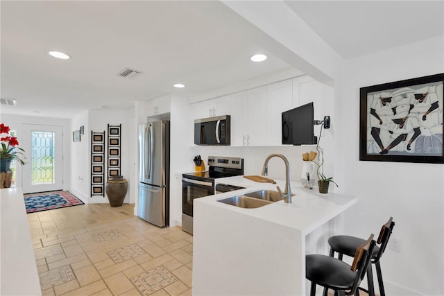 kitchen featuring visible vents, a peninsula, a sink, stainless steel appliances, and a kitchen breakfast bar