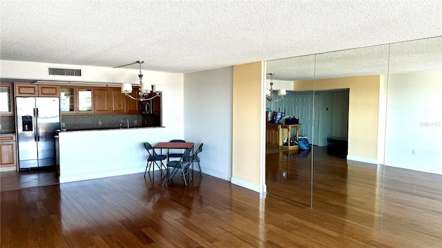 kitchen with dark wood-style flooring, brown cabinets, stainless steel appliances, visible vents, and a chandelier