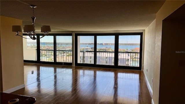 empty room with a wall of windows, an inviting chandelier, wood finished floors, and a healthy amount of sunlight