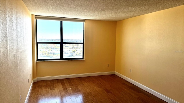 spare room with baseboards, a textured ceiling, and hardwood / wood-style floors