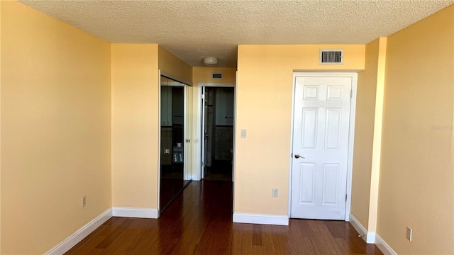 unfurnished bedroom featuring baseboards, a textured ceiling, visible vents, and dark wood-type flooring