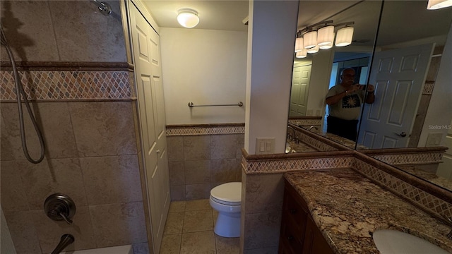 bathroom with toilet, a wainscoted wall, tile patterned floors, bathtub / shower combination, and tile walls