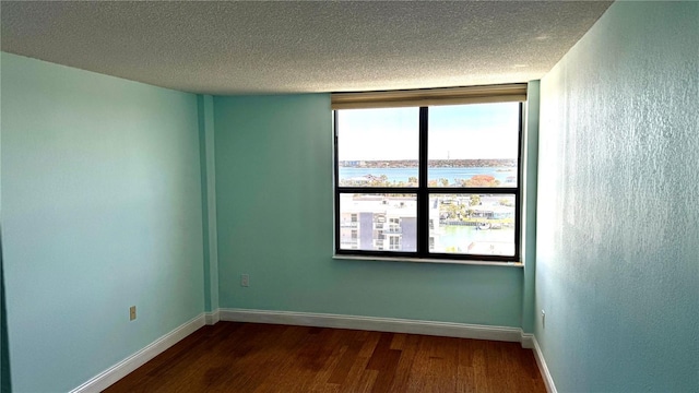 unfurnished room with dark wood-style floors, a textured ceiling, and baseboards