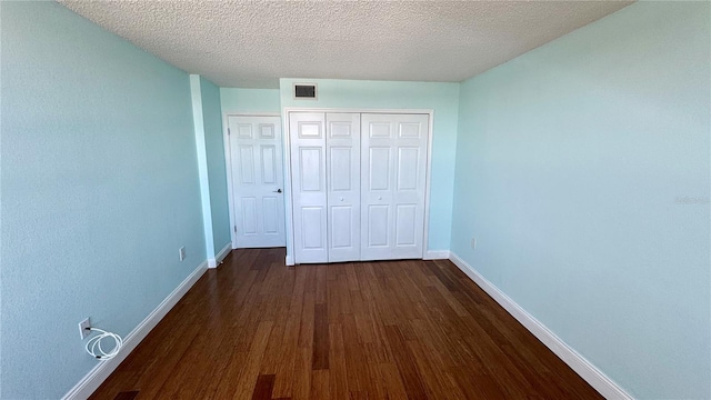 unfurnished bedroom featuring baseboards, visible vents, dark wood-type flooring, a textured ceiling, and a closet