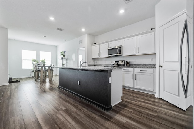 kitchen featuring visible vents, white cabinetry, appliances with stainless steel finishes, light stone countertops, and a center island with sink