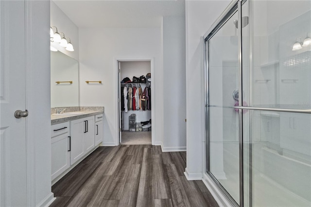 full bathroom featuring a spacious closet, a stall shower, vanity, wood finished floors, and baseboards