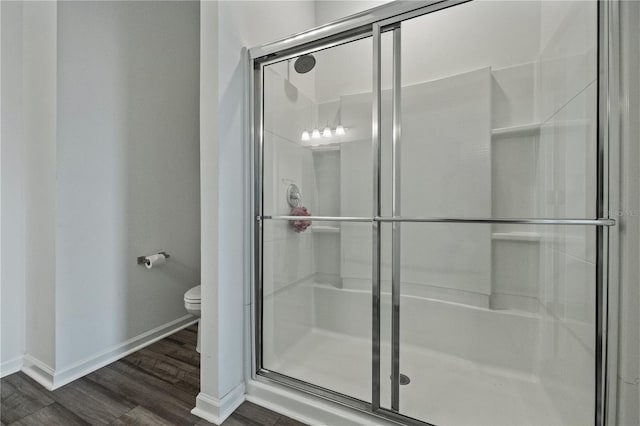 bathroom with toilet, a shower stall, baseboards, and wood finished floors