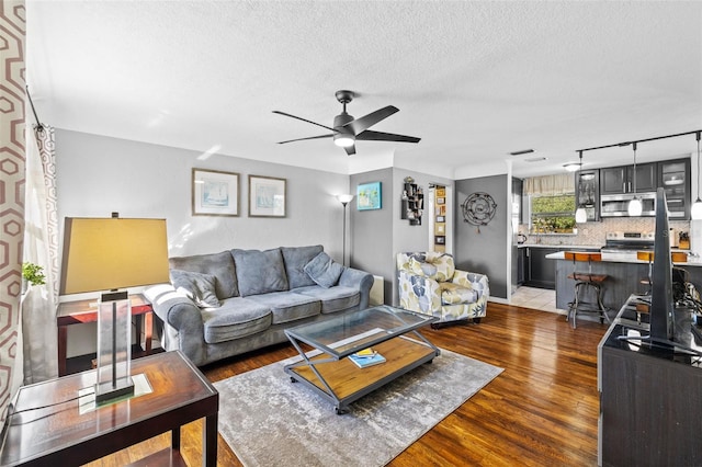 living area with a textured ceiling, a ceiling fan, and wood finished floors