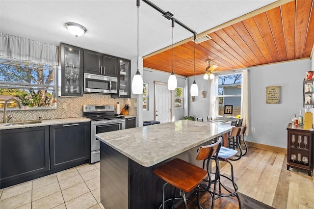 kitchen featuring a sink, stainless steel appliances, wood ceiling, glass insert cabinets, and tasteful backsplash