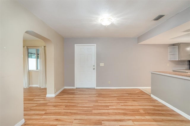 interior space featuring light wood-style floors, arched walkways, visible vents, and baseboards