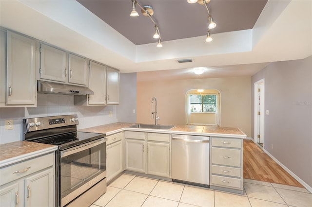 kitchen with stainless steel appliances, light countertops, a sink, and under cabinet range hood