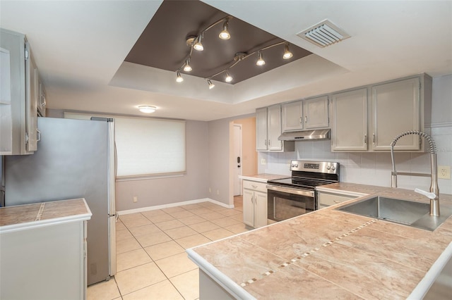 kitchen with a tray ceiling, visible vents, appliances with stainless steel finishes, a sink, and under cabinet range hood