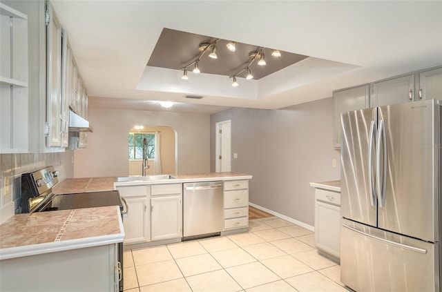 kitchen with a raised ceiling, stainless steel appliances, under cabinet range hood, white cabinetry, and light tile patterned flooring