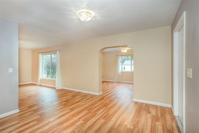 empty room featuring light wood-style floors, arched walkways, baseboards, and a ceiling fan