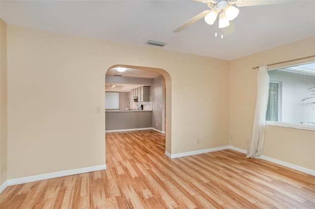 unfurnished room with arched walkways, visible vents, light wood-style flooring, ceiling fan, and baseboards