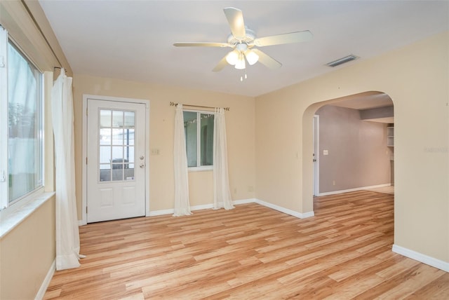 spare room featuring arched walkways, light wood finished floors, visible vents, and baseboards