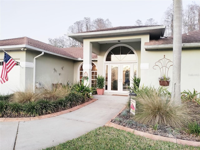 entrance to property featuring french doors, roof with shingles, and stucco siding