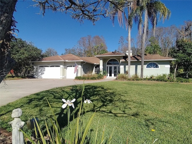 mediterranean / spanish home featuring a garage, concrete driveway, french doors, stucco siding, and a front yard