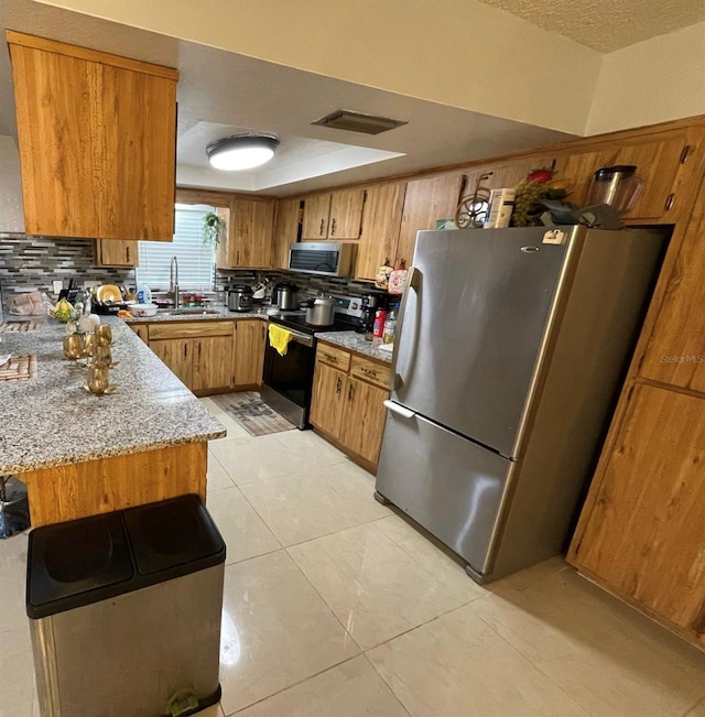 kitchen with sink, light tile patterned floors, stainless steel appliances, light stone countertops, and decorative backsplash