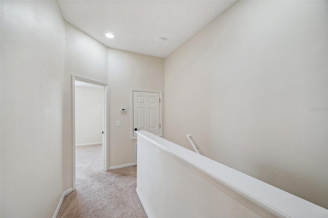 hall featuring baseboards, light carpet, and an upstairs landing