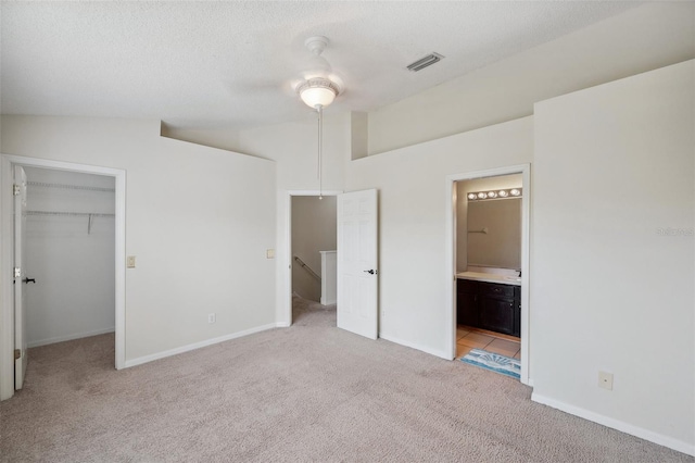 unfurnished bedroom with visible vents, ensuite bath, vaulted ceiling, a walk in closet, and light colored carpet