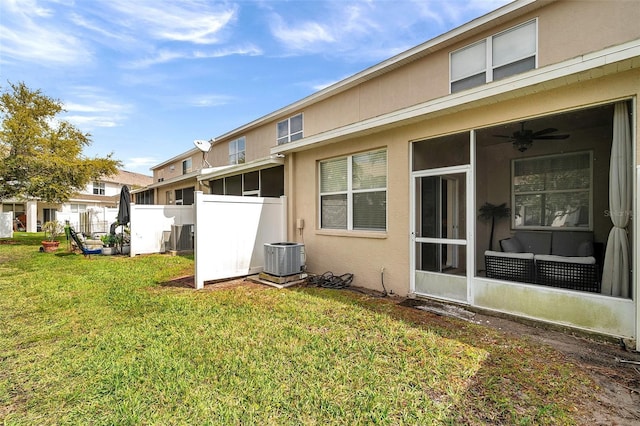 rear view of property featuring fence, central AC, stucco siding, a lawn, and a sunroom