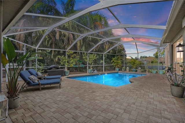 pool at dusk with an outdoor pool, glass enclosure, and a patio